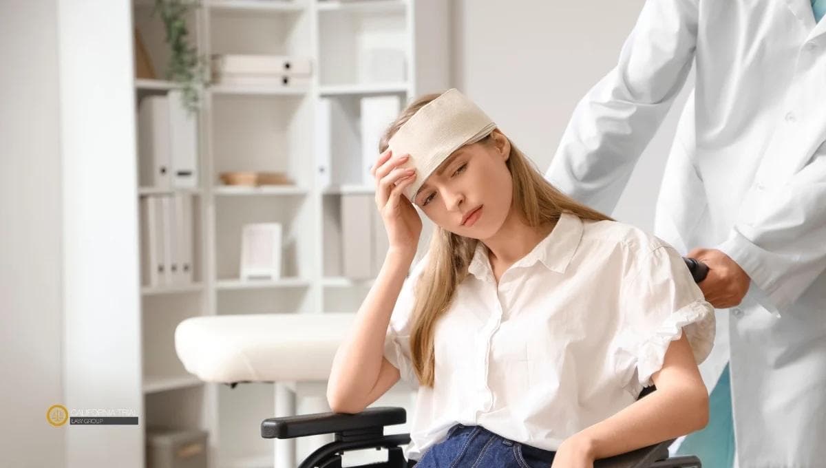 Concussion patient with a head bandage sitting in a wheelchair during a medical consultation, being assisted by a doctor in a clinical setting